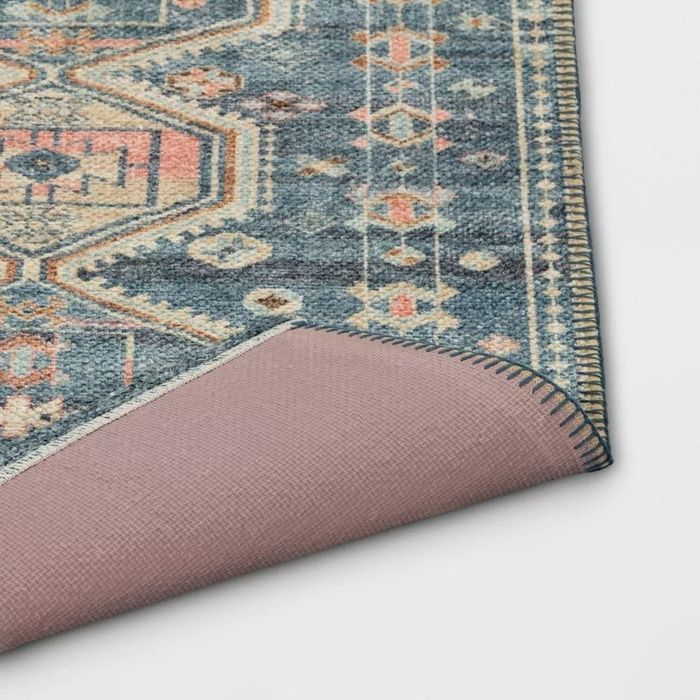 A close-up shot of the corner of a richly patterned rug, slightly lifted to reveal the backing, showcasing the intricate design that's perfect for home decor enthusiasts.
