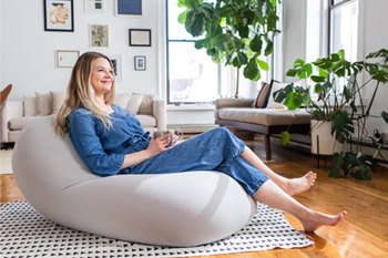 Model lounging reclined on a smooth gray bean bag chair resting on a triangle-patterned rug