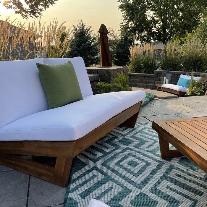two white outdoor loveseats in a backyard, adorned with green and blue pillows