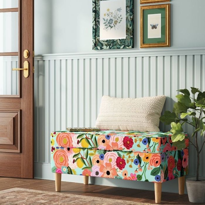 a floral storage bench with a cushion placed in a room featuring framed artwork on the wall and a wooden door
