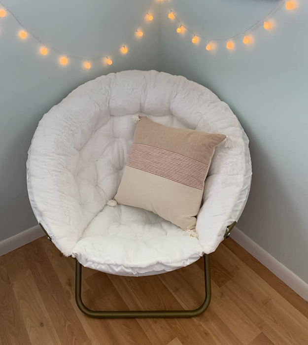 White saucer chair with curved metal foldable legs, tufted faux fur cushion, and a pink and cream throw pillow