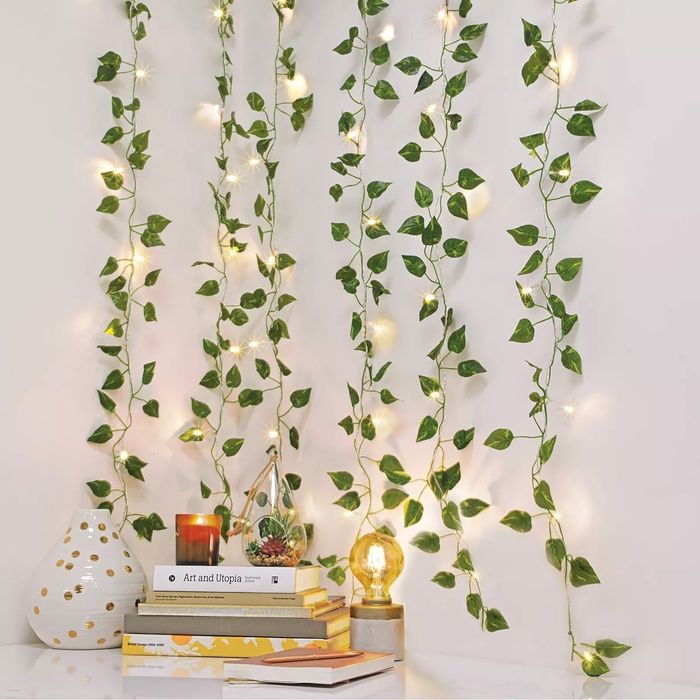 String lights wrapped in artificial ivy, cascading down a wall next to stacked books and a glowing bulb