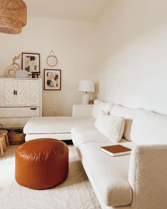 a cream-toned sectional sofa placed beside a warm brown ottoman in a cozy living room