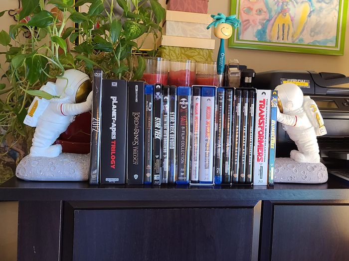 A bookshelf adorned with action figures and a variety of movie DVD cases, including titles like 'Transformers' and 'Fight Club'.
