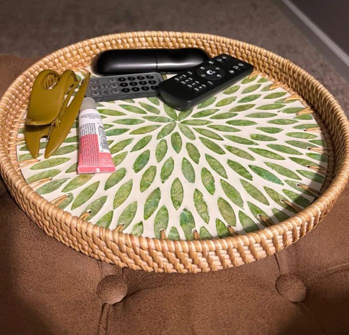 A round decorative tray holding a hair clip, a pink cream tube, and two black remotes, placed on a cushioned surface.