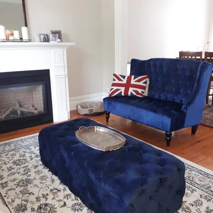 a navy blue tufted loveseat with a matching ottoman and a Union Jack pillow for a stylish touch