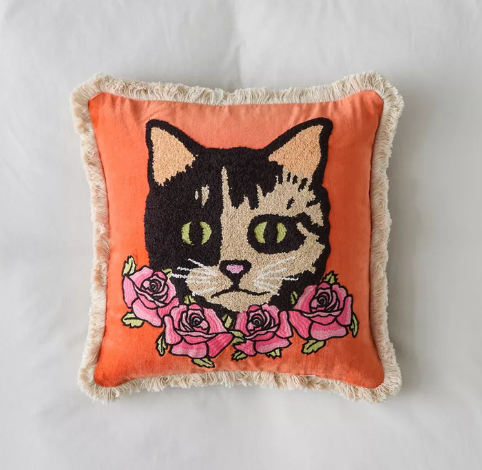 A decorative pillow with a cat’s face surrounded by roses, adding a playful and charming touch to your home decor.