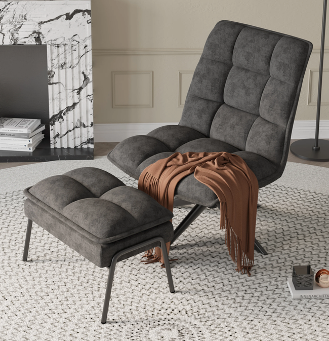 Gray tufted plush curved lounge chair without armrests and a matching ottoman set on a round white rug