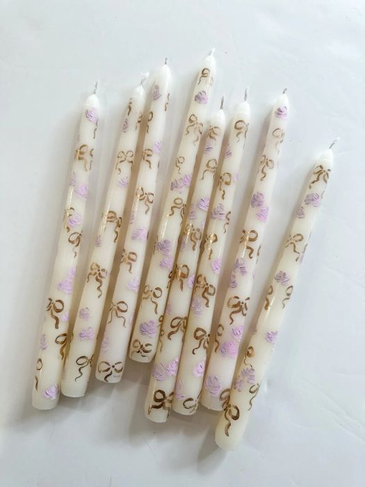 A set of eight decorative candles adorned with gold and pink floral designs, neatly arranged on a white surface