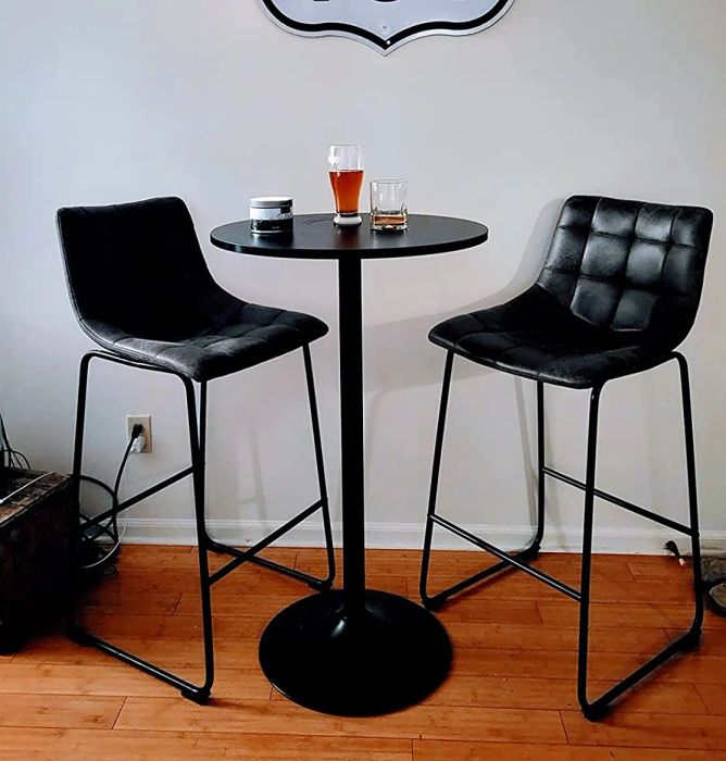 a reviewer's photo of a small black high-top table with drinks placed on it, surrounded by two black stools