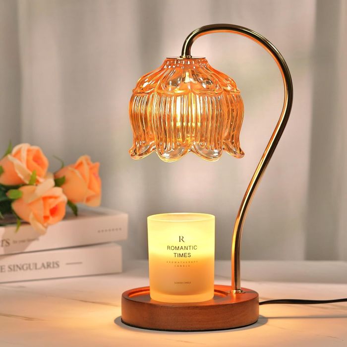 A gold-stemmed lamp with a flower-shaped bulb casting light over a warming candle