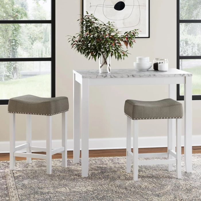 A contemporary kitchen setup featuring a white table with a marble top, two gray cushioned bar stools, and a plant centerpiece. Minimalist artwork adorns the wall