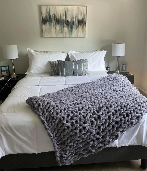 A soft grey knitted blanket draped across a bed.