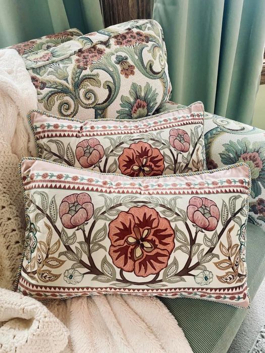Two embroidered throw pillows with floral designs rest on a patterned armchair, draped with a soft, light-colored blanket.