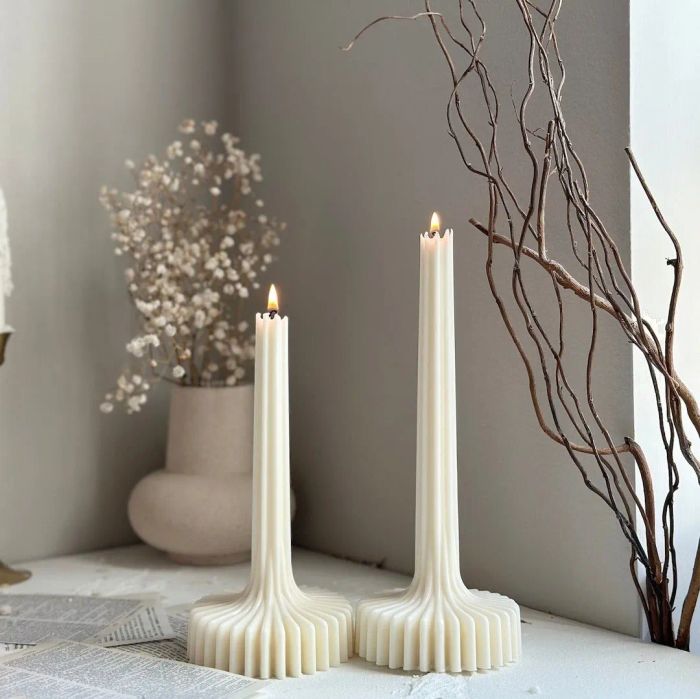 Two sculptural tapered candles with textured bases placed on a table.