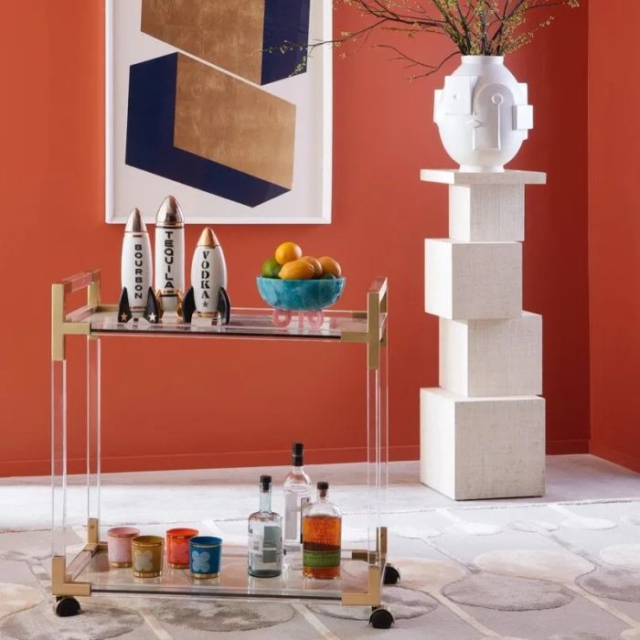 A sleek modern bar cart adorned with artistic decor, including a geometric piece, a sculpture, and an assortment of bottles and glasses placed on and around the cart.