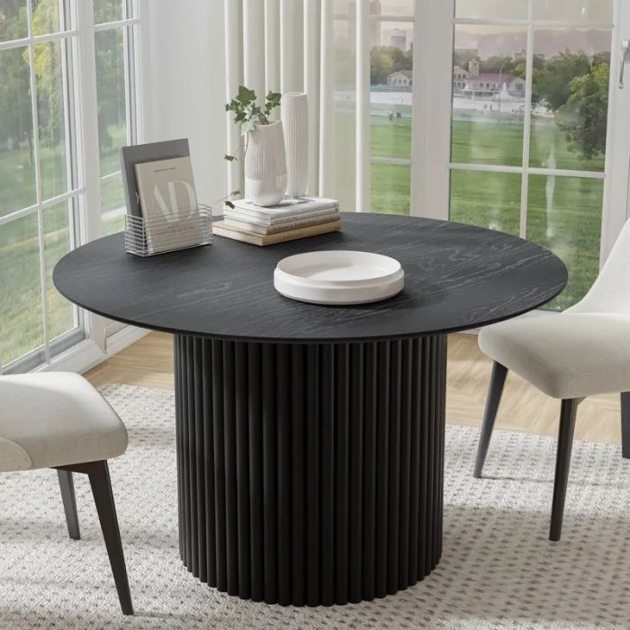 A modern round black dining table with decorative pieces, surrounded by two upholstered chairs in a well-lit room with expansive windows