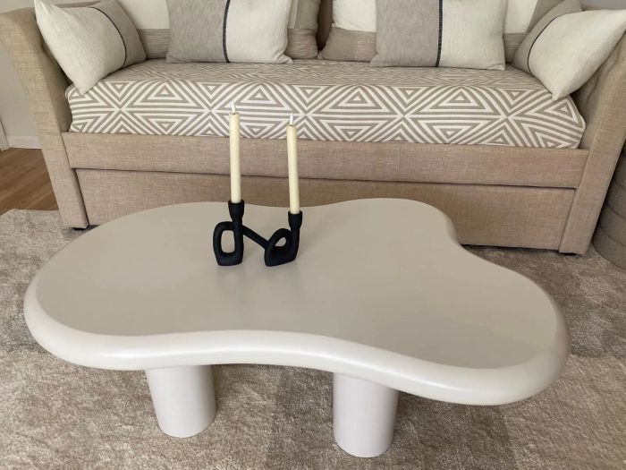 A chic beige couch adorned with geometric-patterned cushions and a sleek, modernist white coffee table with two black candleholders holding white candles.