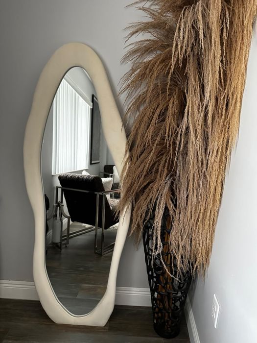 A full-length mirror beside a textured decor piece in a modern interior, reflecting a home office setup