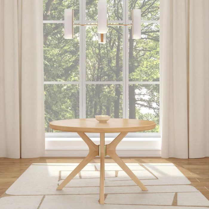 A sleek round wooden dining table with minimalist design, set in front of a window with a scenic view of nature, accompanied by a hanging light fixture.