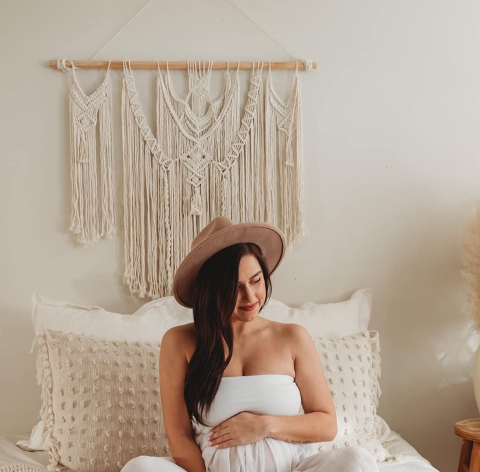 A reviewer poses in front of the macrame wall hanging above their bed.
