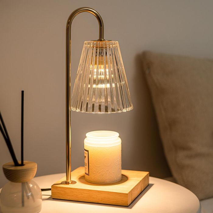 A sleek table lamp with a ribbed glass shade, set on a modern wooden base, beside a white candle.