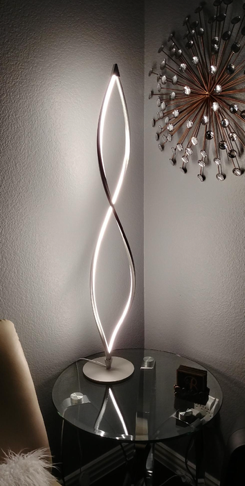 A modern, stylish spiral table lamp with LED light, resting on a glass side table in a chic corner of a room.