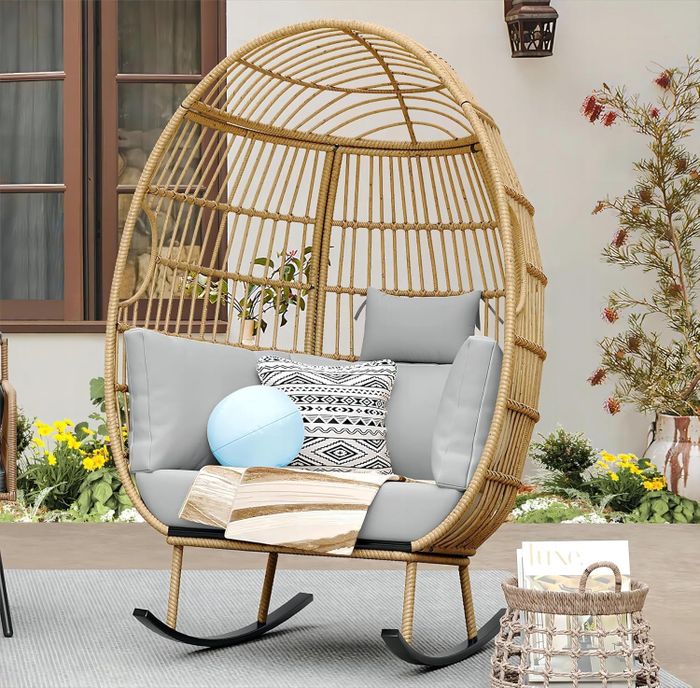 A wicker egg chair in the backyard, complete with comfy cushions