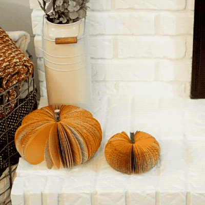 A model placing a large pumpkin made from books on a white fireplace.