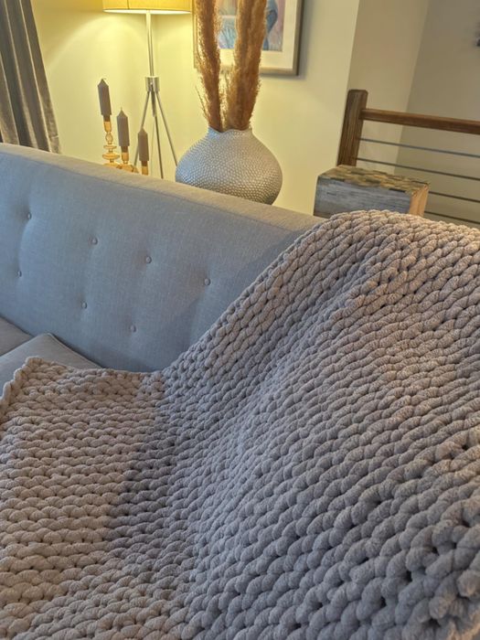 Another reviewer’s sandstone-colored chunky blanket casually draped over a couch in a chic living room setting