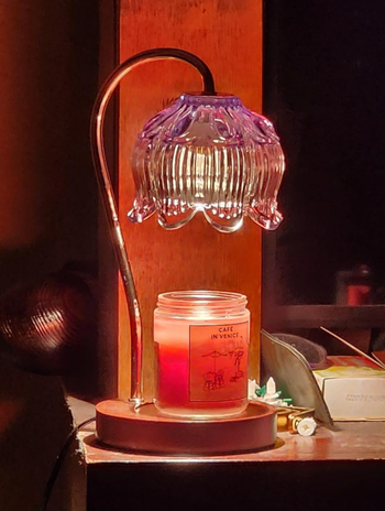 A glass lamp with a scalloped shade softly illuminates a partially burned candle labeled.