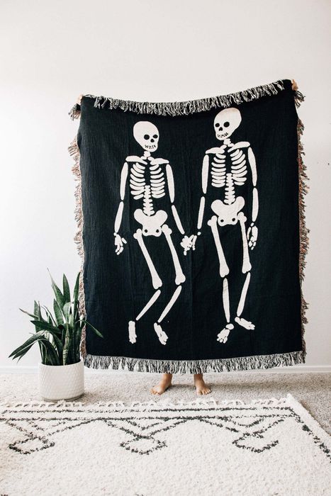 a woven throw rug in black with tassels and two skeletons printed on the front