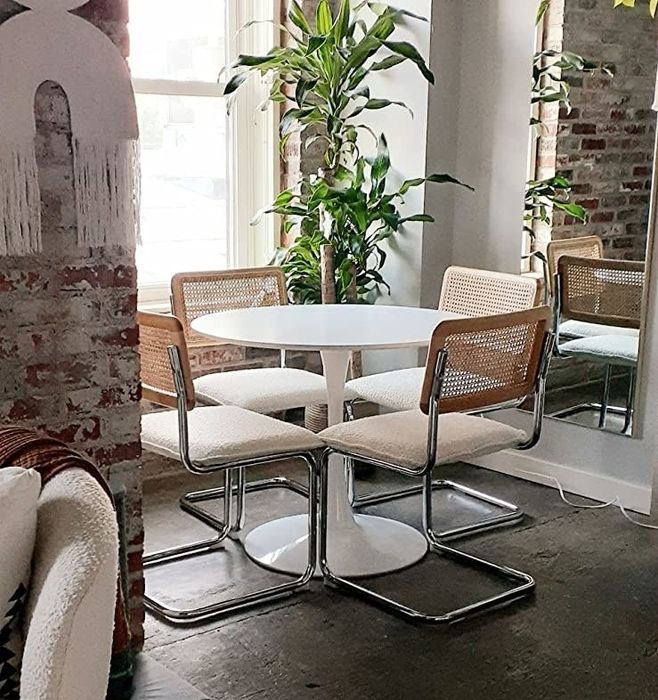 The reviewer displays four chairs with white cushions neatly arranged under their round dining table.