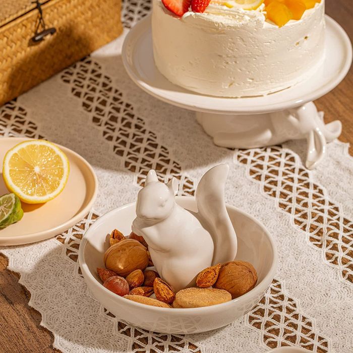 a white dish with a ceramic squirrel at its center, filled with nuts