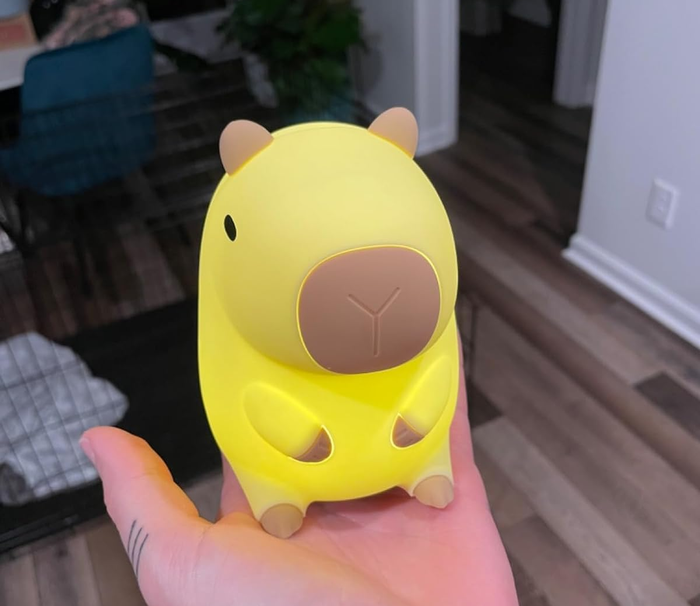 A person holding a small yellow capybara nightlight in their hand