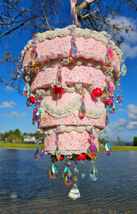 A whimsical pink cake-shaped chandelier with hanging crystals