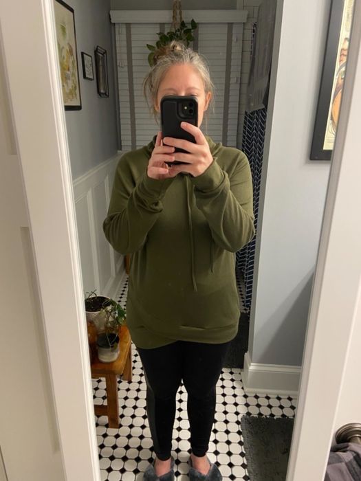 A person is taking a mirror selfie in a casual outfit, featuring a khaki green tunic, leggings, and slippers, embodying a laid-back look.
