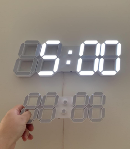 A reviewer holds the 9.5-inch version of the clock, with the 15-inch version displayed on the wall behind them.