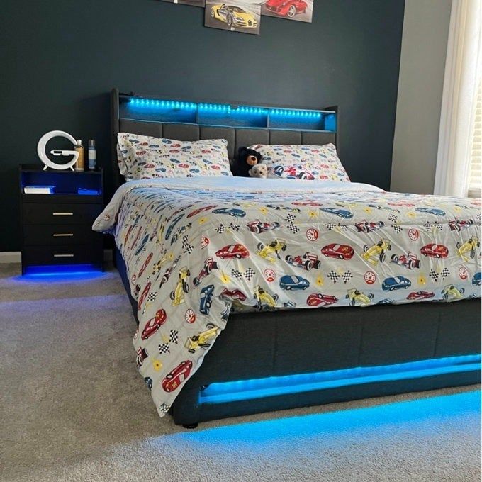 A bedroom featuring race car-themed bedding, an illuminated headboard, and a bedside table. Perfect for a child’s room with a fun, automotive flair.