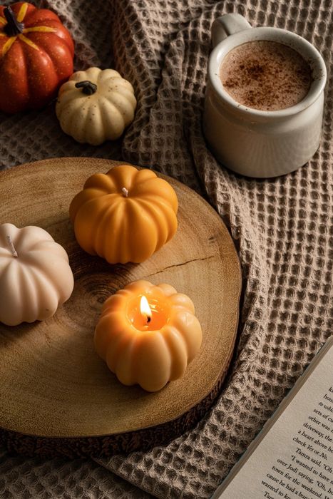 a small pumpkin-shaped candle with a stem, its wick unlit, resting on a wooden tray next to matching candles