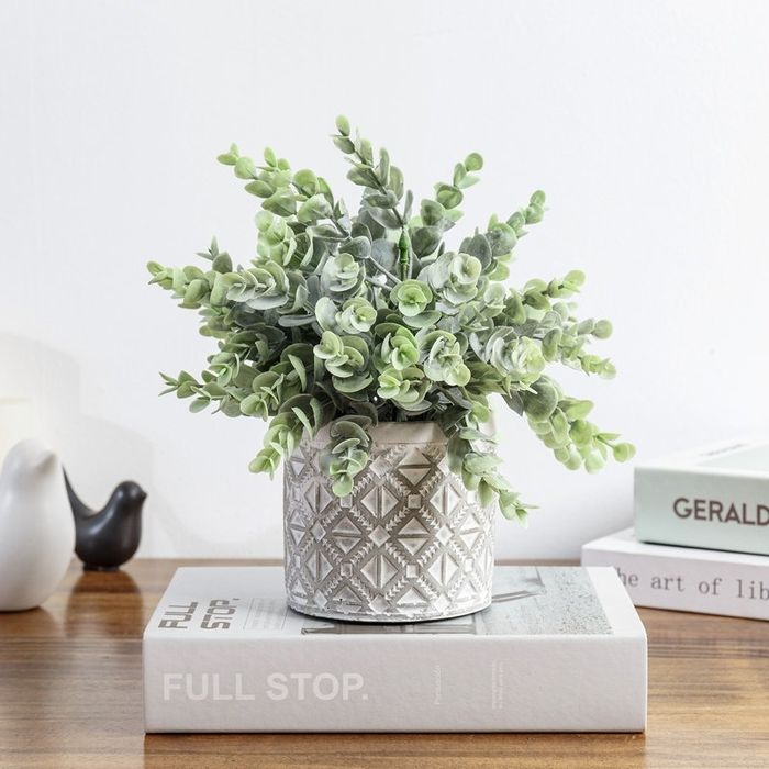 The faux eucalyptus plant placed in a ceramic pot on a table.