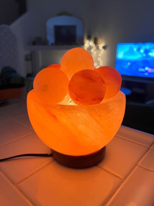 A Himalayan salt lamp with glowing salt spheres sitting on a counter, casting a warm, ambient glow in a cozy living room setting.