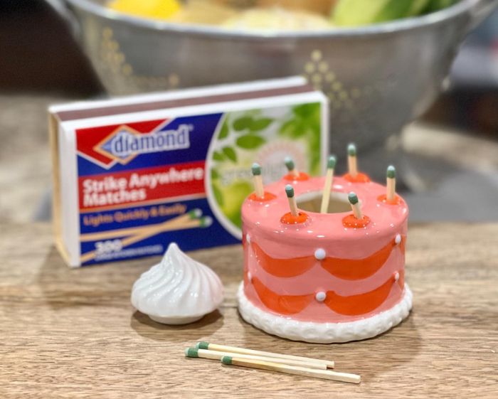 A mini ceramic cake-shaped match holder with matches placed like candles