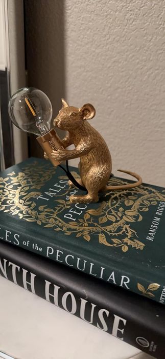 A charming gold-painted mouse lamp holding a glowing light bulb.