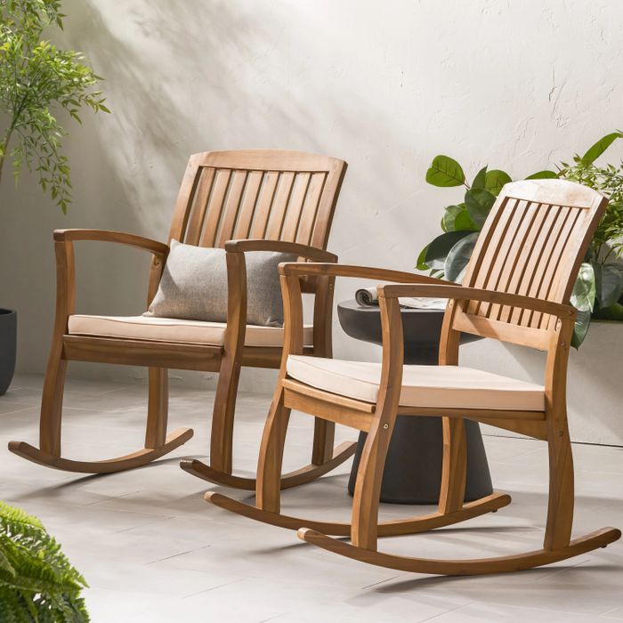 Two wooden rocking chairs with soft cushions on a patio, surrounded by lush green plants