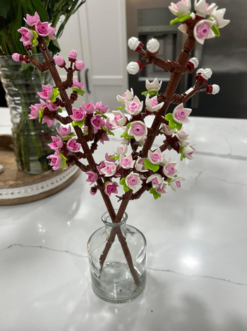 Lego flowers in shades of pink and white arranged in a glass vase on a kitchen counter