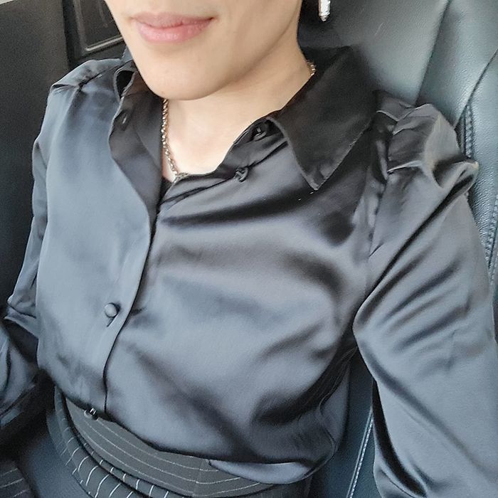 Person wearing a black satin blouse, accessorized with delicate jewelry.