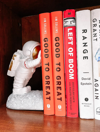 An astronaut figurine standing proudly, holding up books on a shelf, as noted by reviewers.