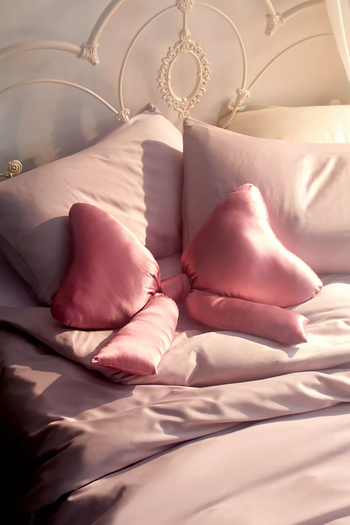 A bed adorned with assorted satin decorative pillows, including two heart-shaped ones and a roll-style pillow, perfect for home decor enthusiasts.