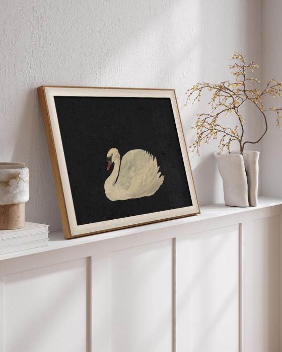 A framed painting of a graceful swan resting on a shelf, next to a vase with delicate twigs, all set in a cozy home ambiance.